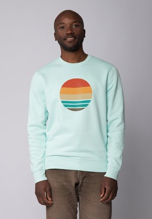 Light mint green sweatshirt featuring a circular graphic with orange, yellow, teal, and brown stripes. Ribbed cuffs and crew neck design.