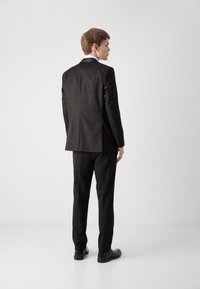Czarny garnitur z teksturowanym wzorem, slim fit, jednorzędowa marynarka i dopasowane spodnie. Polerowane czarne buty dopełniają całość.