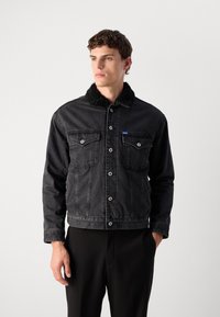 Chaqueta de mezclilla negra con un cuello de sherpa, presenta cierres de botón, dos bolsillos en el pecho y un diseño ajustado.