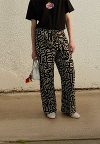 Παντελόνι με φαρδιά μπάρα σε μαύρο και λευκό μοτίβο με ρυθμιζόμενο κορδόνι στη μέση, συνδυασμένο με μαύρο μπλουζάκι και λευκή τσάντα χεριού. Ορατά  παπούτσια με επίπεδη σόλα.