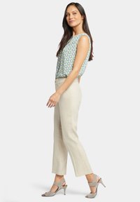 Bezramenná vzorovaná blůza v modré a zelené barvě, kombinovaná s béžovými kalhotami rovného střihu a světlými šedými sandály na podpatku.