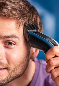 Tagliacapelli con un design ergonomico nero e blu, dotato di impugnatura texturizzata e lunghezza della lama regolabile, in uso su capelli corti.