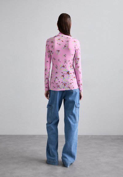 Langsleeve top in roze met abstracte meerkleurige patronen, gecombineerd met losse blauwe denim cargobroeken met zijzakken.