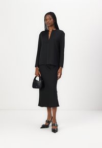 Blusa nera a maniche lunghe con scollatura a V, abbinata a una gonna midi coordinata. Include tacchi a punta con dettagli a fibbia e una borsa a tracolla piccola.