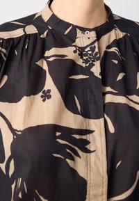 Gros plan d'un chemisier noir et beige avec un imprimé floral et un petit col mandarin boutonné.