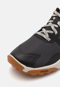 Black athletic shoe with a mesh upper, textured overlays, and light gray laces. Features a brown rubber outsole with "Contagrip" branding.