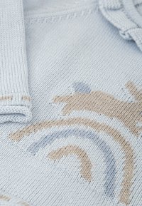 Tejido de punto azul claro con patrones en tonos beige y azul suave. Presenta bordes acanalados, mostrando una textura suave y un diseño detallado.