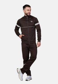 Ensemble de survêtement marron avec des rayures blanches, veste zippée et pantalons à taille élastique. Présente un logo sur la poitrine et des poches latérales.