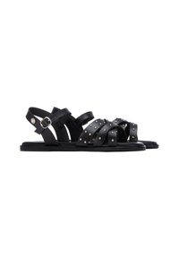 Sandalias de cuero negro con múltiples correas entrecruzadas, detalles con tachuelas y una correa ajustable con hebilla en el tobillo. Suela plana, diseño minimalista.