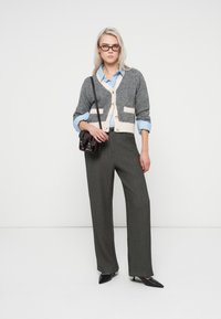 Gray and cream cardigan with pockets over a blue striped shirt, paired with gray wide-leg trousers and black pointed-toe heels, accessorized with a dark bag.