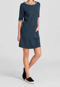 Robe en coton bleu marine à manches trois-quarts, avec des poches latérales et un col rond, associée à des chaussures noires à enfiler.