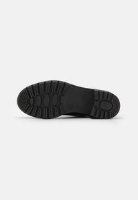Suola di scarpa in gomma nera con motivo di battistrada multidirezionale. Presenta aperture circolari e ovali per una migliore presa e flessibilità.