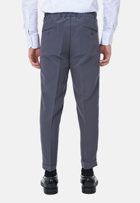 Pantaloni grigi con vita elastica, dotati di due tasche posteriori con chiusura a bottone e orli rifiniti. Indossati con scarpe nere.
