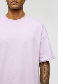 Lichtpaarse katoenen t-shirt met een ronde hals en korte mouwen. Heeft een relaxte pasvorm en een zachte textuur. Opvallende tatoeage op de onderarm.
