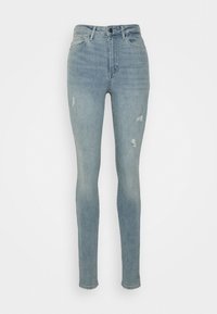 Jeans skinny de denim azul claro con cintura alta, que presentan zonas desgastadas y pequeños parches rasgados para un aspecto usado. Textura suave.