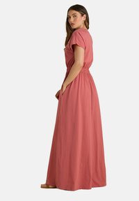 Robe maxi en corail, avec des manches courtes, une taille élastique, des poches latérales et une silhouette fluide. Tissu doux et léger.