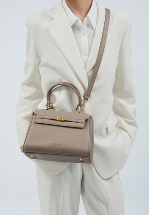 Borsa a mano in pelle grigia con forma strutturata, ferrature dorate e tracolla rimovibile, tenuta da una persona in abito bianco.