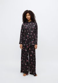 Ensemble de pyjama floral noir comprenant une chemise à boutons à manches longues et un pantalon à jambes larges, orné de petits motifs floraux roses et verts.