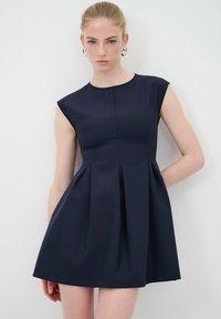 Tummansininen ilmanhiha dressi, jossa on tiukka vartalo-osa ja pleated-hame. Valmistettu sileästä kankaasta, jossa on pyöreä kaula-aukko ja minimalistinen muotoilu.