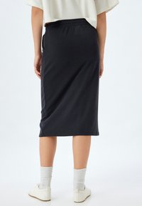 Sort midi-skirt lavet af blødt stof, med elastisk talje. Glat tekstur med lige snit, der når ned til under knæene.