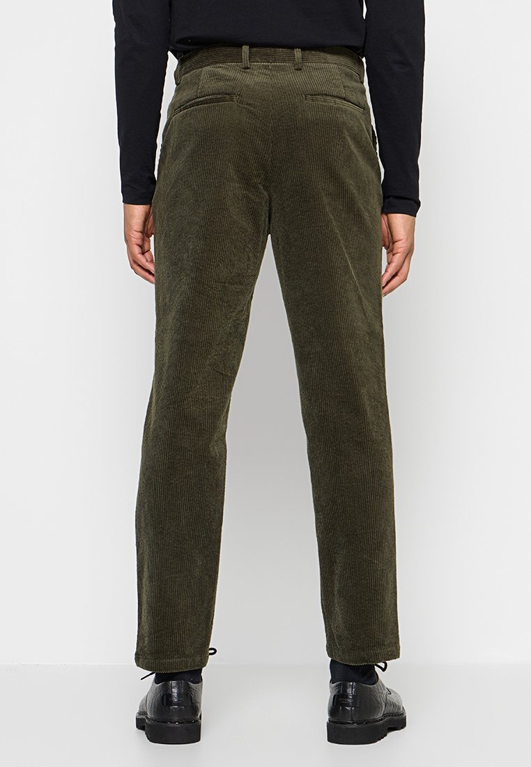 Grüne Cordhosen mit geradem Schnitt und Gesäßtaschen, mit vertikaler Rippung und glatter Textur. Kombiniert mit schwarzen Schuhen.