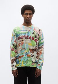 Πολύχρωμο πλεκτό πουλόβερ με μίγμα πράσινων, μπλε και πορτοκαλί σχεδίων, με έντονο κείμενο "UNBREAKABLE" και αφηρημένα μοτίβα. Στρογγυλή λαιμόκοψη.