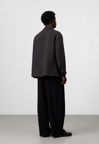 Ciemnoszara wełniana kurtka o luźnym kroju, z jedną szwem na plecach, noszona na czarnych szerokich spodniach i czarnym obuwiu. Gładka faktura.