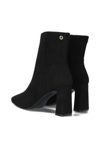 Schwarze Wildleder-Stiefeletten mit Blockabsatz, spitzem Fuß und einem goldenen Akzentknopf auf der Rückseite. Glatte Textur und ein elegantes Design.