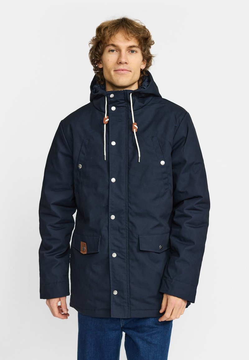 Marinblå huvjacka med dragkedja och tryckknappar, två framfickor samt krämfärgade dragsnören med bruna detaljer.