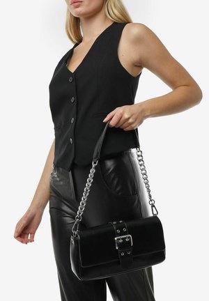 Black leather handbag with a rectangular shape, featuring a buckle detail, chain strap, and smooth texture. Worn by a model in black attire.