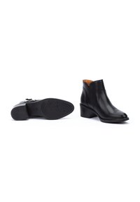 Botines de cuero negro con tacón bajo, que presentan un diseño elegante, textura suave y un interior marrón que contrasta. Detalle de cordones visible.