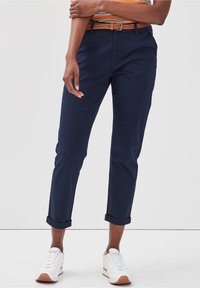 Marina chinos med uppvridna fållar, gjorda av bomull. Kombinerat med ett vävt brunt bälte och vita sneakers med bruna accenter.