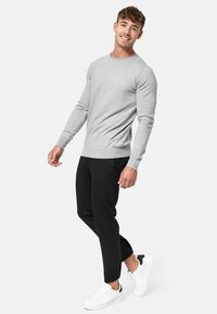 Suéter gris claro de manga larga con puños y dobladillo acanalados, combinado con pantalones negros ajustados y zapatillas blancas con acentos negros.