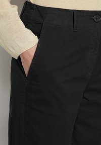 Černé kalhoty z hladkého materiálu, s boční kapsou a zapínáním na knoflík v pase. Design je upraven tak, aby měl slim fit.