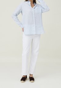 Camicia a righe azzurro chiaro con bottoni, pantaloni bianchi e espadrillas marroni scure. La camicia ha una tasca e colletto, il tessuto appare morbido.