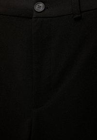 Close-up van zwarte stof met een knop en gestikte naad details op op maat gemaakte broek of pantalons.