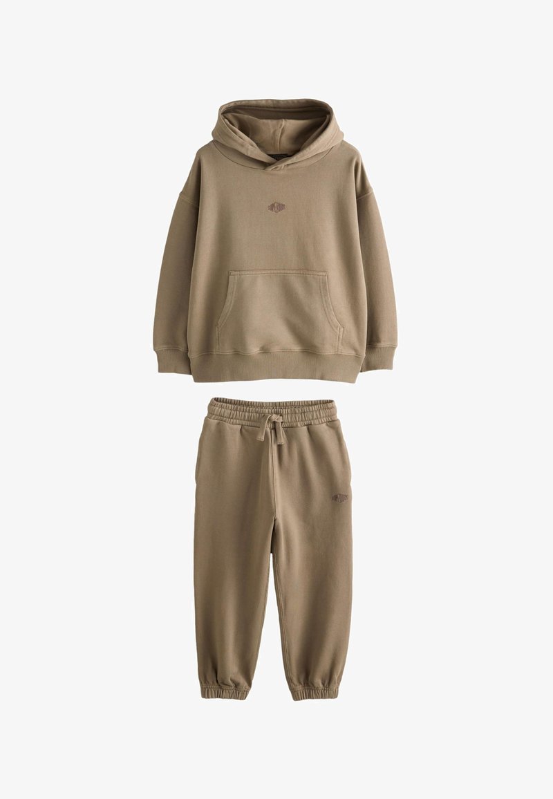 Sweat à capuche beige avec poche sur le devant et pantalon jogger assorti à cordon de serrage, avec poignets élastiques et broderie discrète du logo.