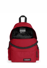 Sac à dos en nylon rouge avec un compartiment principal zippé, une poche avant et des finitions noires. Il est doté d'une poignée en tissu et de bretelles rembourrées.