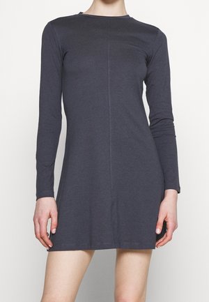 Femme portant une robe cintrée gris foncé à manches longues, longueur au genou, avec une couture centrale à l'avant, se tenant devant un fond blanc.