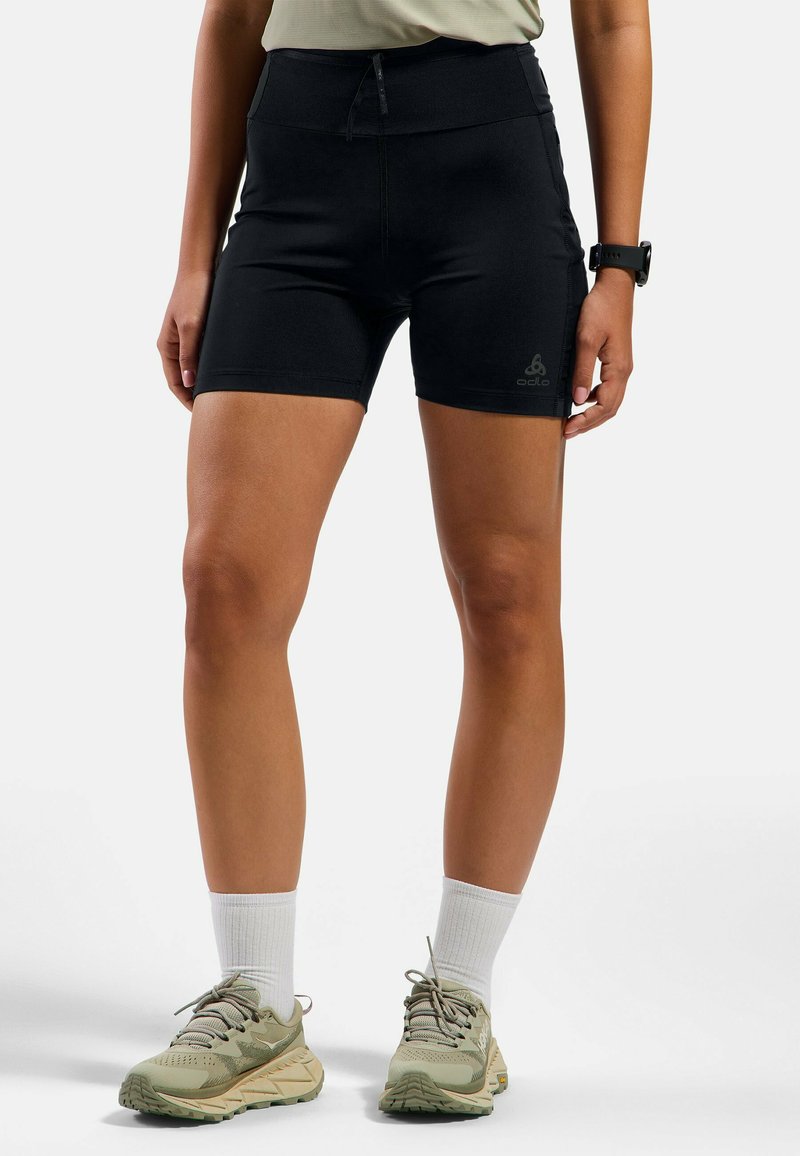 Zwarte sportshorts met een hoge tailleband, voorzien van een ritssluiting aan de voorkant en een logo-detail. Gecombineerd met olijfgroene sportschoenen en witte sokken.