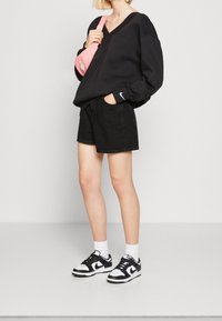 Zwarte sweatshirt met een V-hals, gecombineerd met zwarte denim shorts. Accessoires omvatten een roze schoudertas en zwart-witte sneakers.