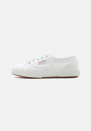 Weißer flacher Canvas-Turnschuh mit Gummisohle, Metallösen und dem Markenlabel "Superga" an der Seite, von der Außenseite gezeigt.