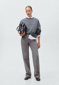 Siva oversize pulover z dolgo rukavom preko bele srajce s kragnico, v kombinaciji z ohlapnimi sivimi jeansom z dodelano šablono. Dopolnjeno s črno torbo.