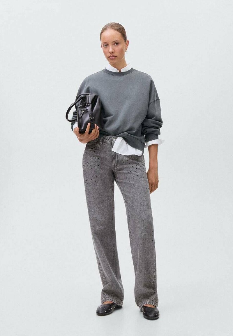 Siva oversize pulover z dolgo rukavom preko bele srajce s kragnico, v kombinaciji z ohlapnimi sivimi jeansom z dodelano šablono. Dopolnjeno s črno torbo.