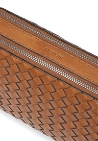 Brun vävd läderpouch med två silverfärgade dragkedjor och "SADDLER" präglat på lädret nära den övre kanten.