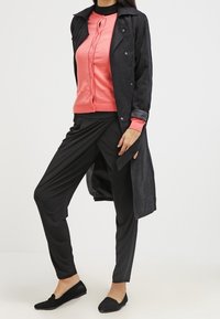 Svart lång kappa över en korallfärgad cardigan, matchad med svarta byxor och svarta platta skor. Släta texturer med ett lagerdesign och knappar.