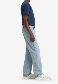 T-shirt à manches courtes bleu marine associé à un jean bleu clair. Les chaussures sont blanches avec des accents gris. Le tissu semble doux, et le jean a une coupe ample.