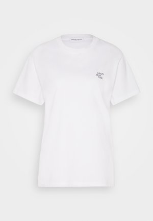 Osoba ubrana w białą koszulkę z napisem "Crazy Sexy Cool" oraz wysokim stanem poszarpane szorty dżinsowe, stojąca na zewnątrz z rękami w kieszeniach.