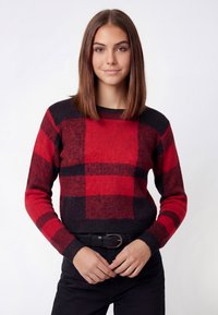 Red and black plaid sweater in a soft knit with a crew neck, ribbed cuffs, and waistband. Paired with black pants and a belt.