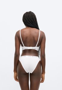 Biely podprsenkový set a nohavičky s vysokým pásom, ktoré majú tenké ramienka a logo na elastickej páske. Hladký materiál s minimalistickým dizajnom.